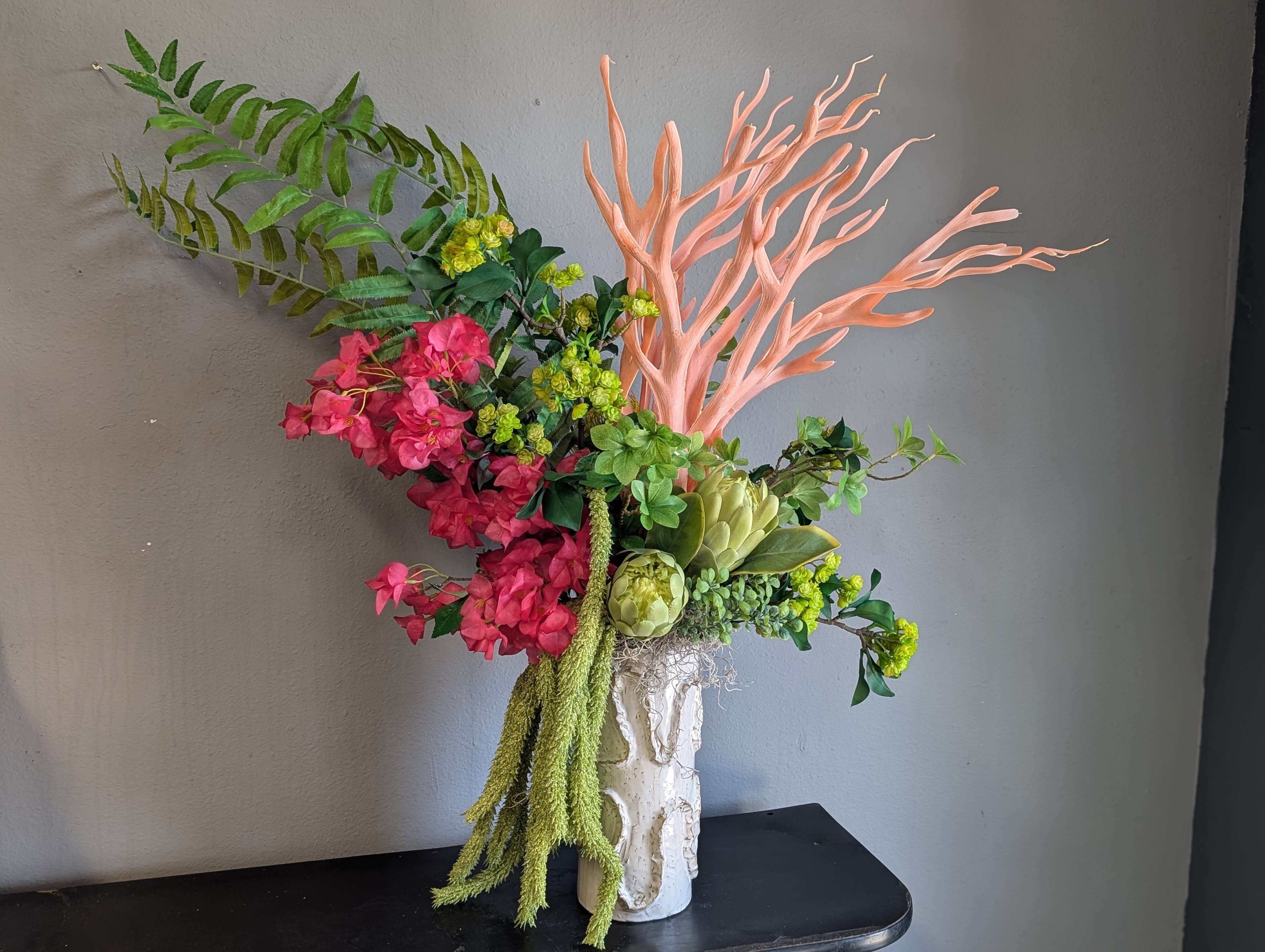 Pink and green floral arrangement in a white vase with coral branches