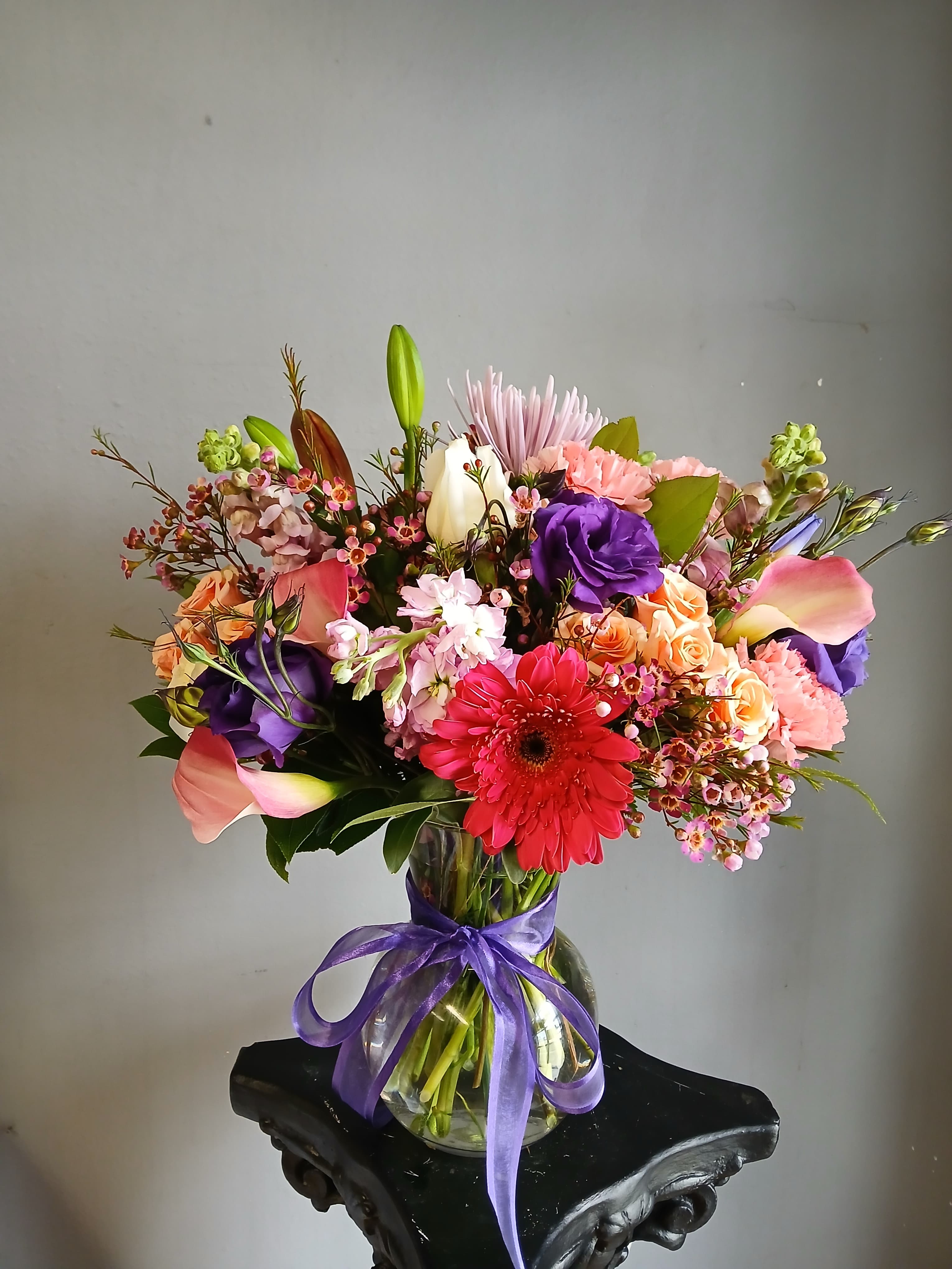 Colorful mixed bouquet in a glass vase tied with a purple ribbon