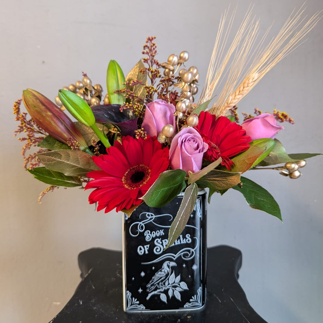 Red gerbera daisies and pink roses in a black vase with decorative wheat stems.