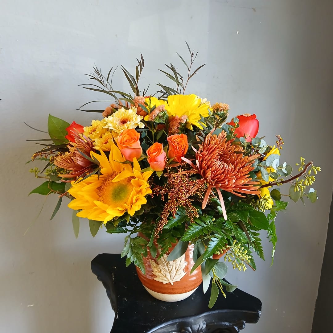 Bouquet of sunflowers, orange roses, and chrysanthemums in a ceramic vase