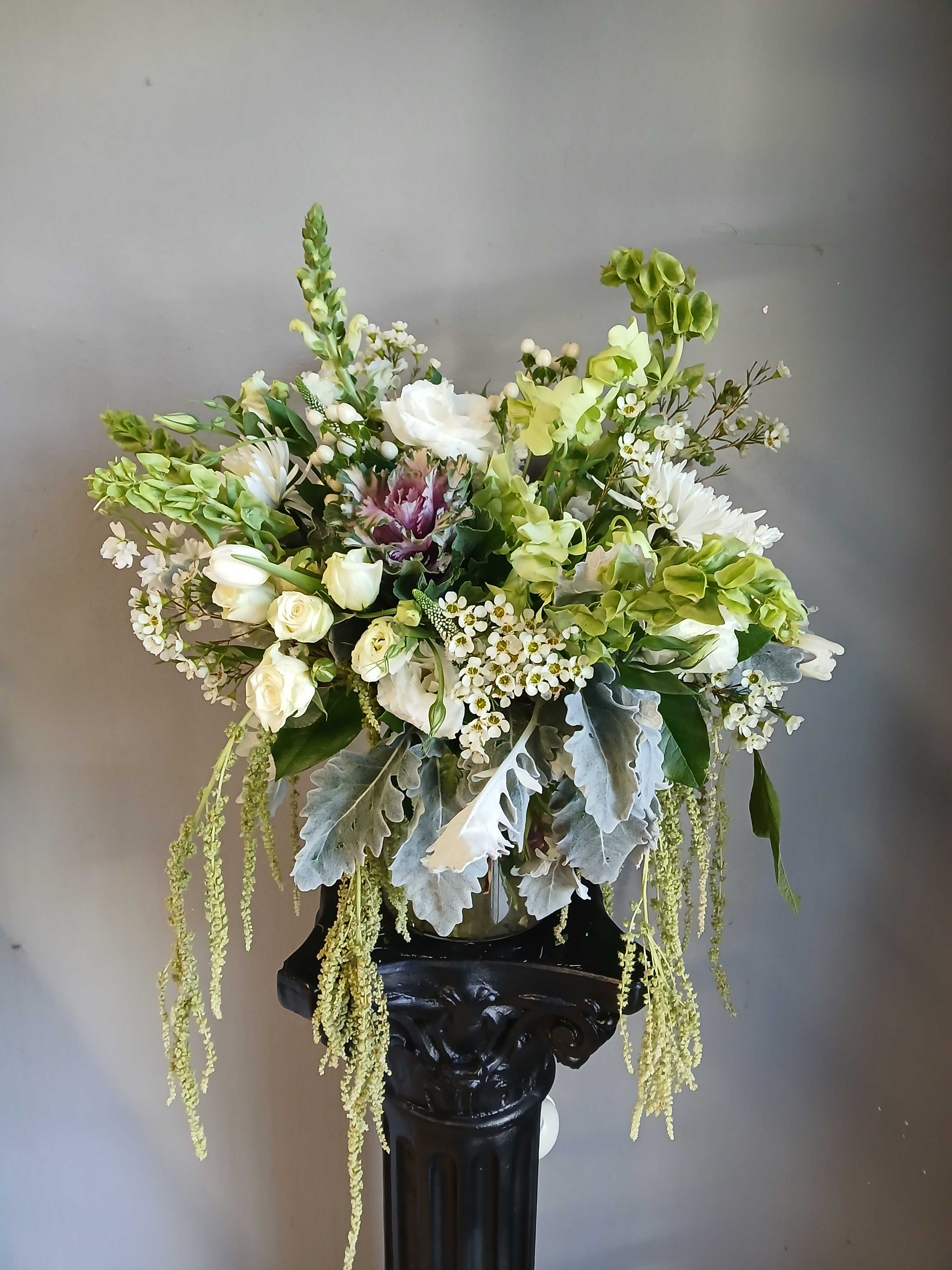 White and green floral arrangement in a glass vase on a pedestal