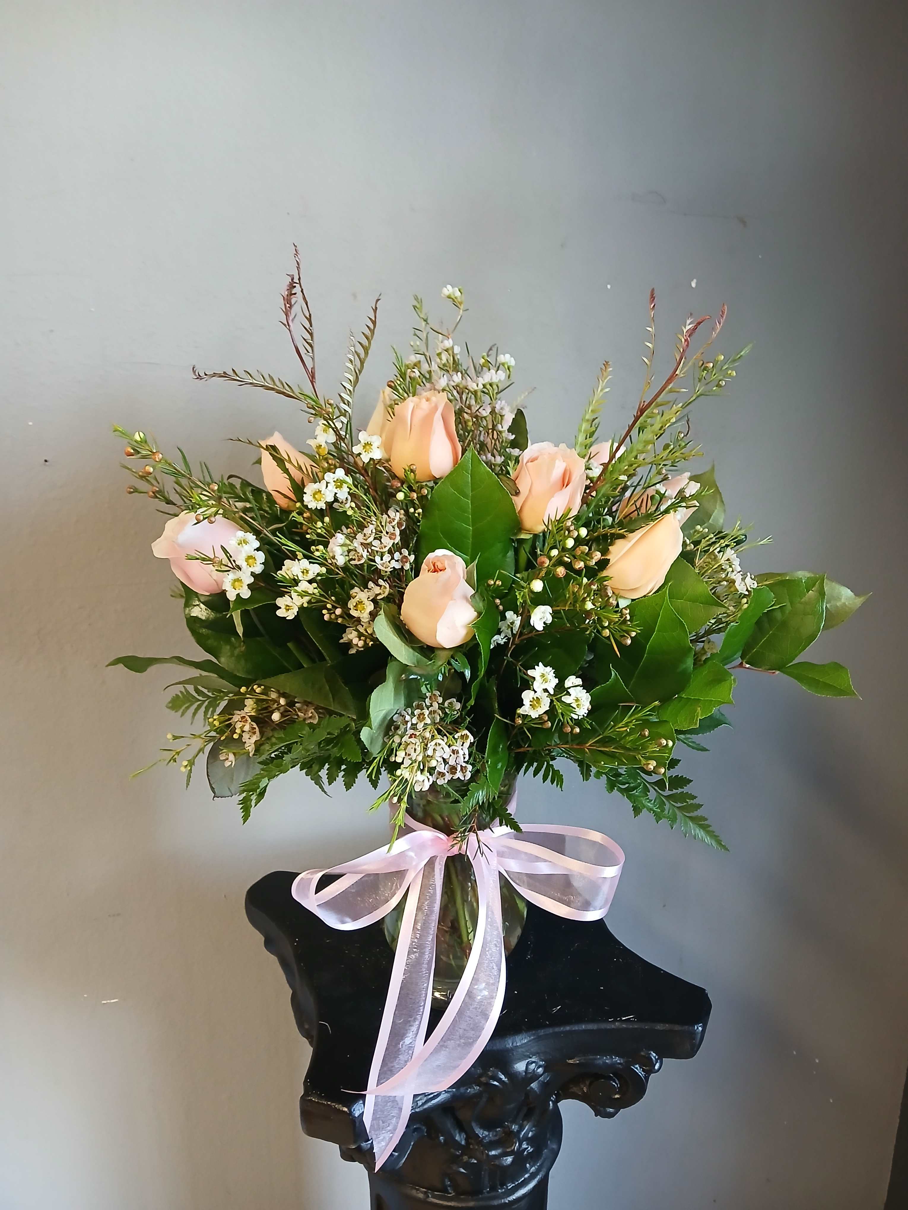 Peach roses in a glass vase with a pink ribbon bow