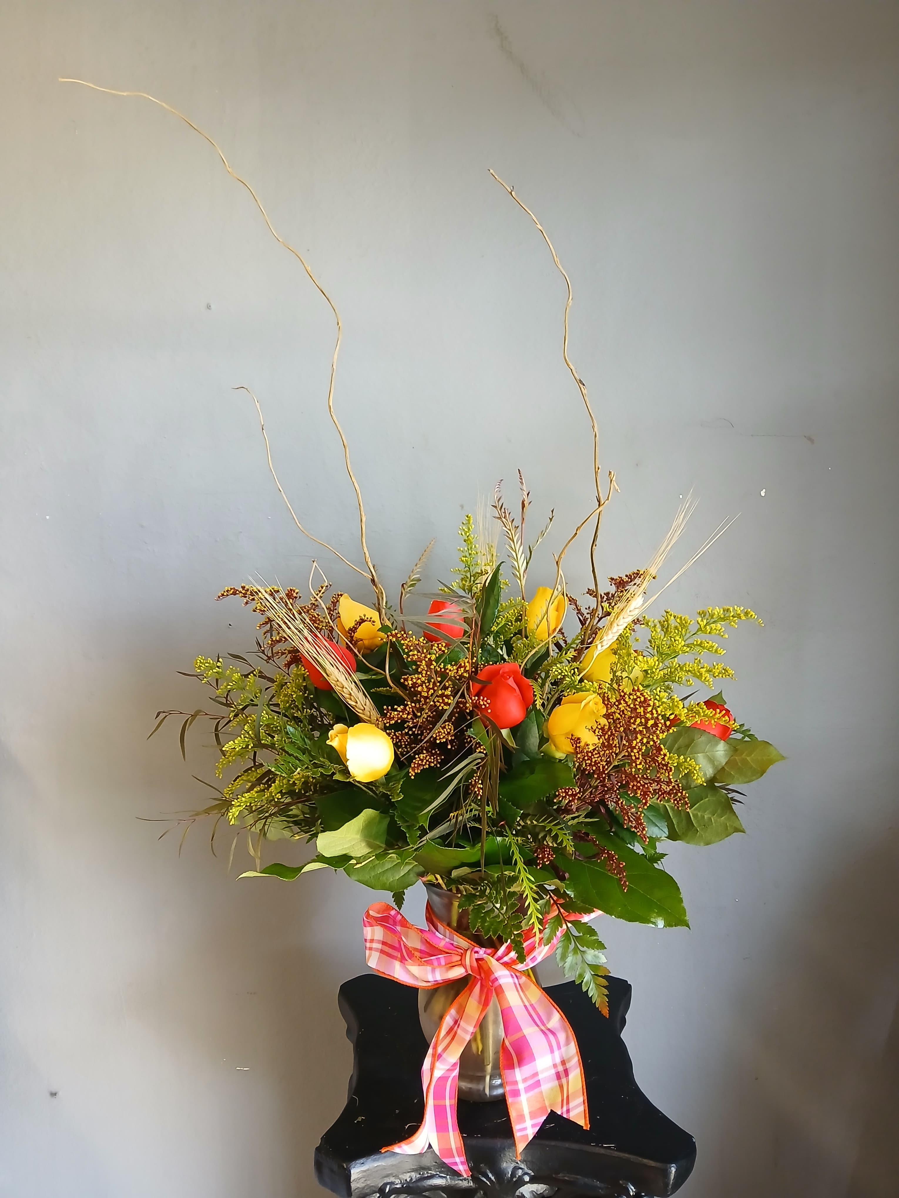 Mixed bouquet of red and yellow roses in a vase with a plaid ribbon