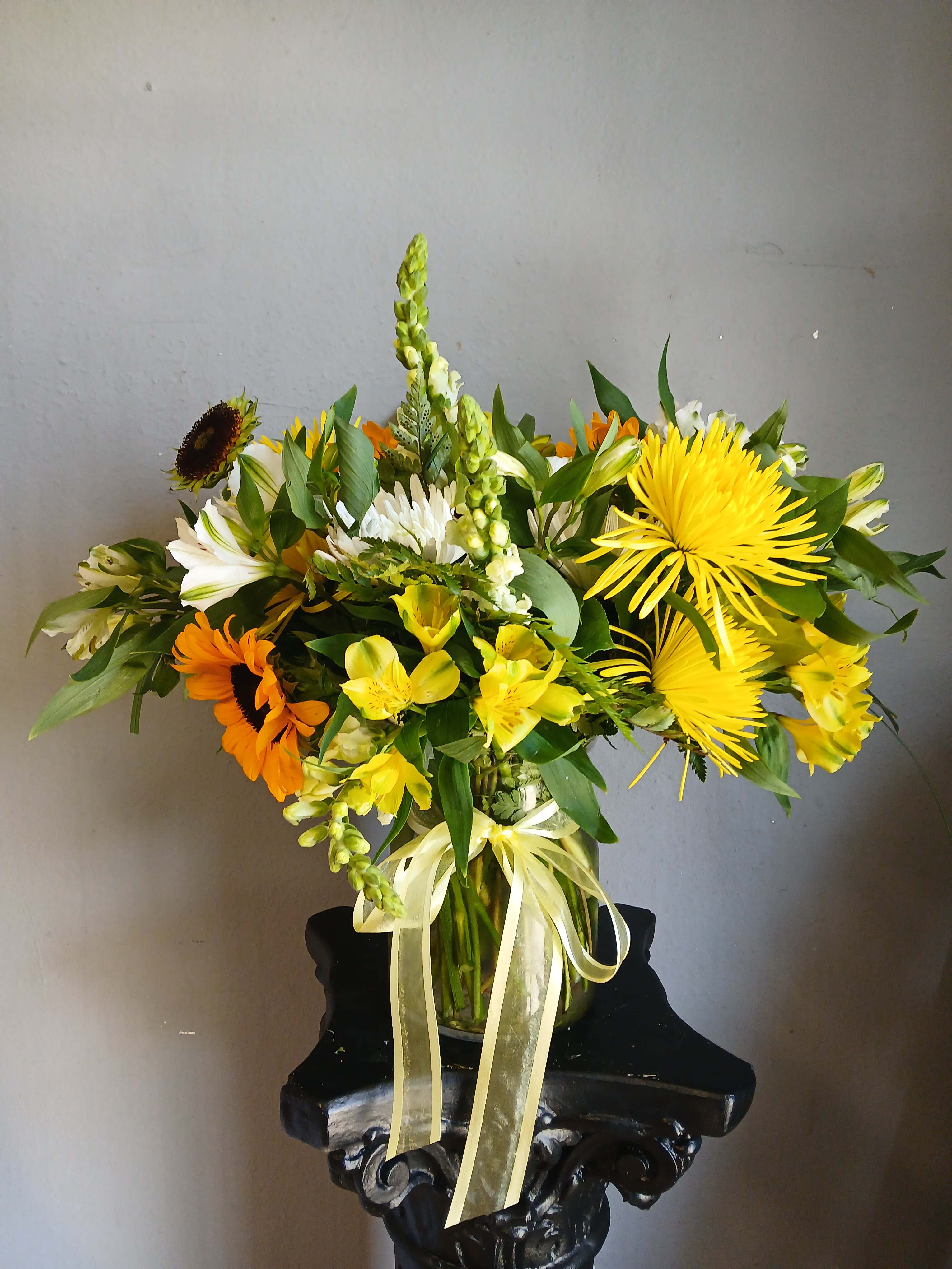 Mixed yellow, white, and orange flowers arranged in a glass vase with a ribbon