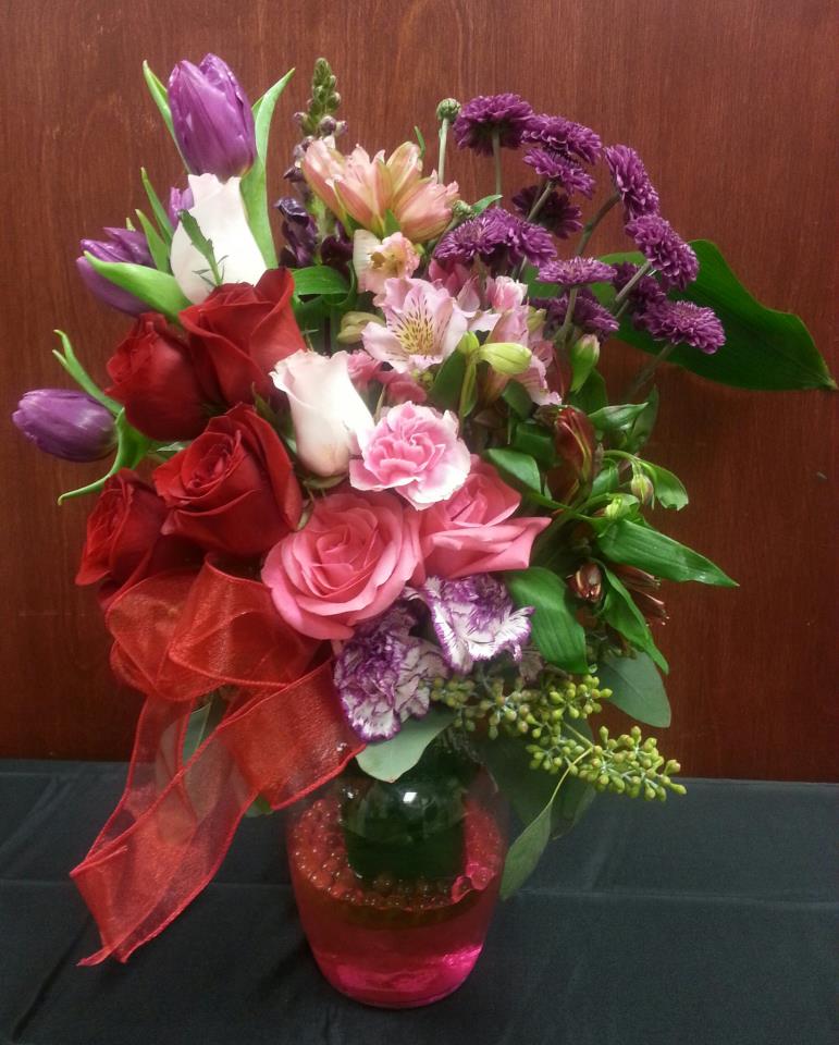 Bouquet of roses, tulips, and purple flowers in a pink glass vase