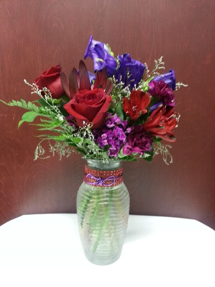 Mixed bouquet of red, purple, and blue flowers in a glass vase