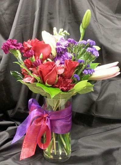 Mixed bouquet of red roses, lilies, and purple flowers in a glass vase