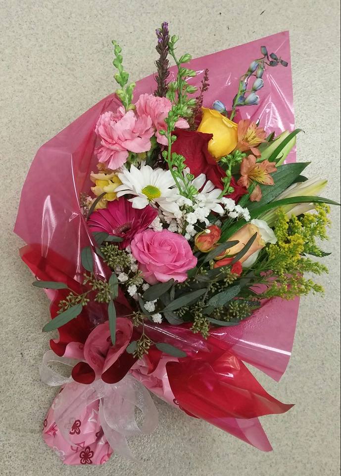 Mixed bouquet of pink, red, yellow, and white flowers wrapped in pink paper
