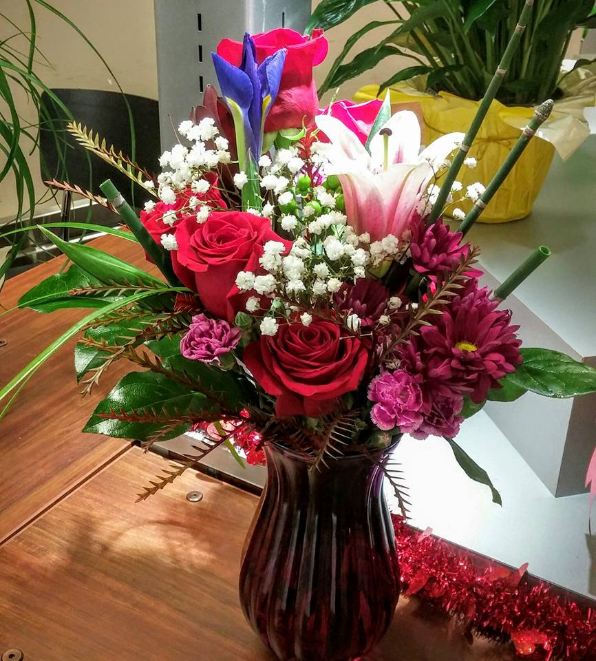 Mixed bouquet of roses, lilies, and daisies in a dark glass vase