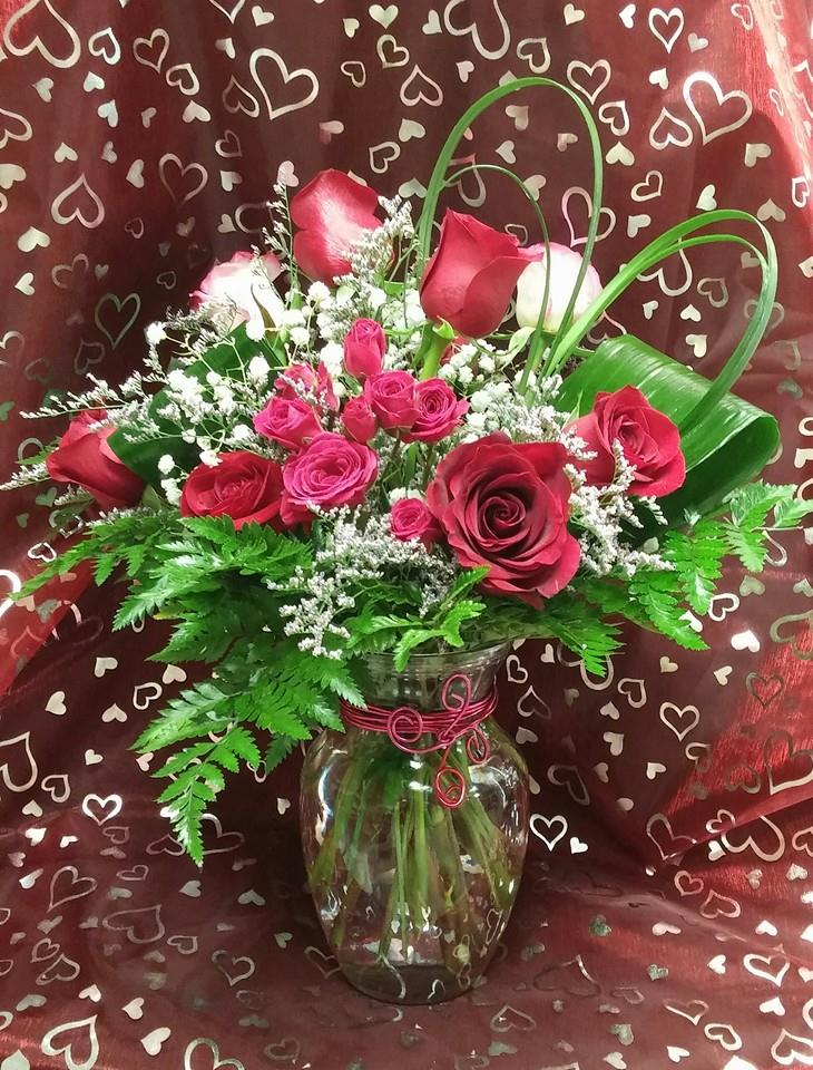 Red and pink roses arranged in a glass vase with heart-patterned wrap