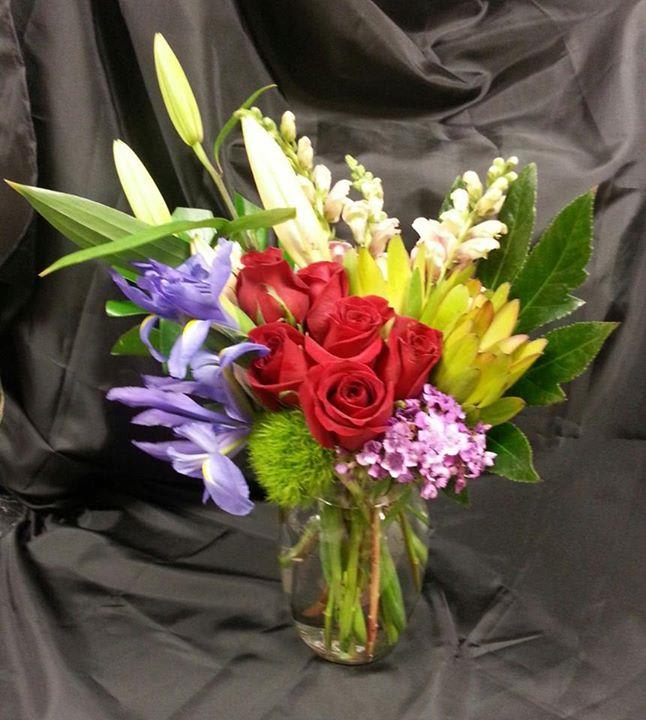 Bouquet of red roses, lilies, and purple flowers in a glass vase