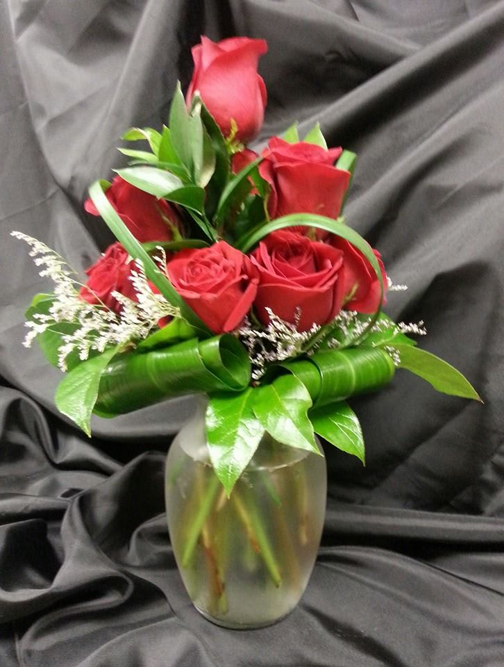 Red roses arranged in a glass vase with green ribbon accents