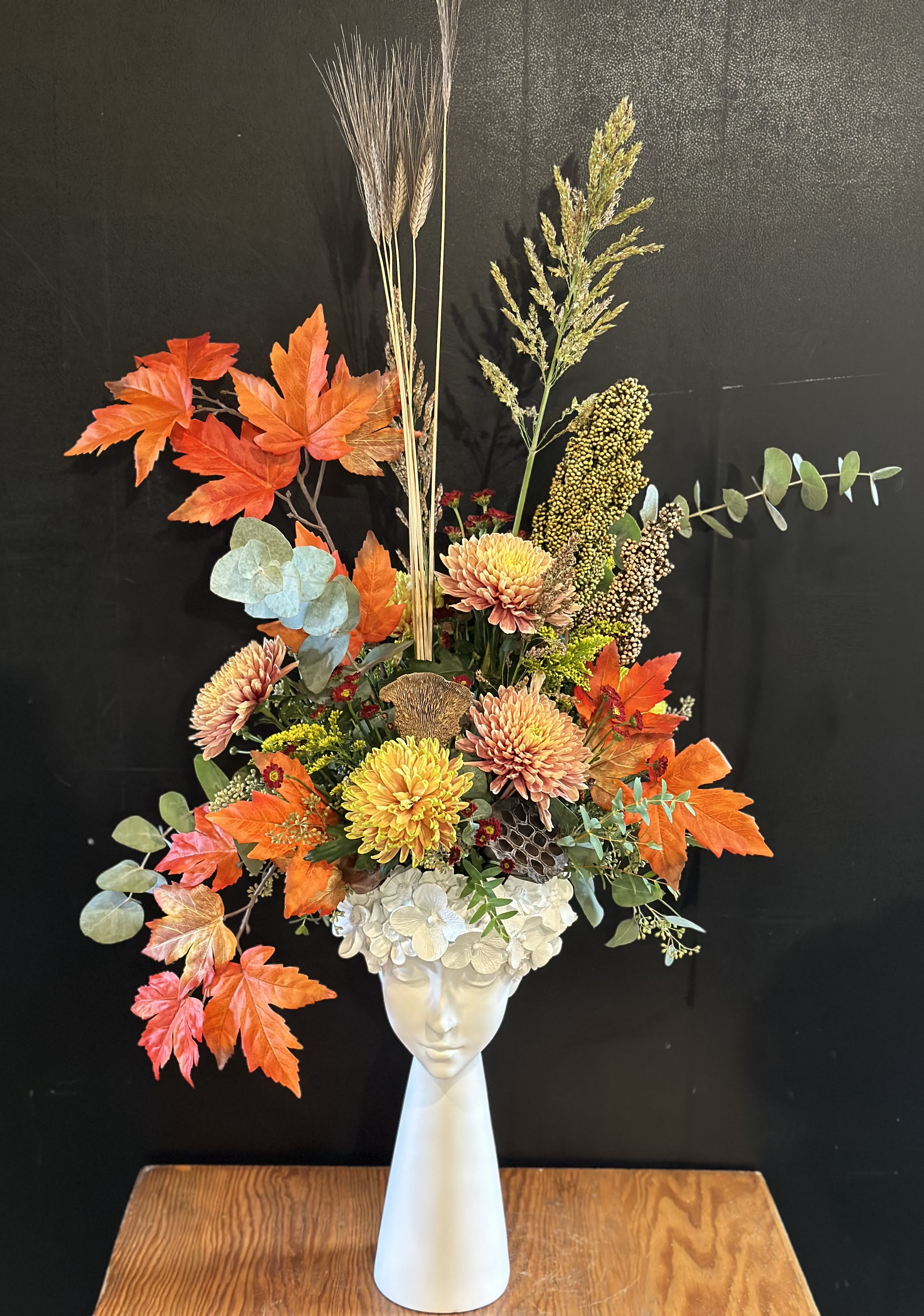 Autumn floral arrangement in a white vase with orange leaves and chrysanthemums