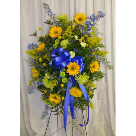 Standing floral spray with yellow blooms and blue ribbon on an easel