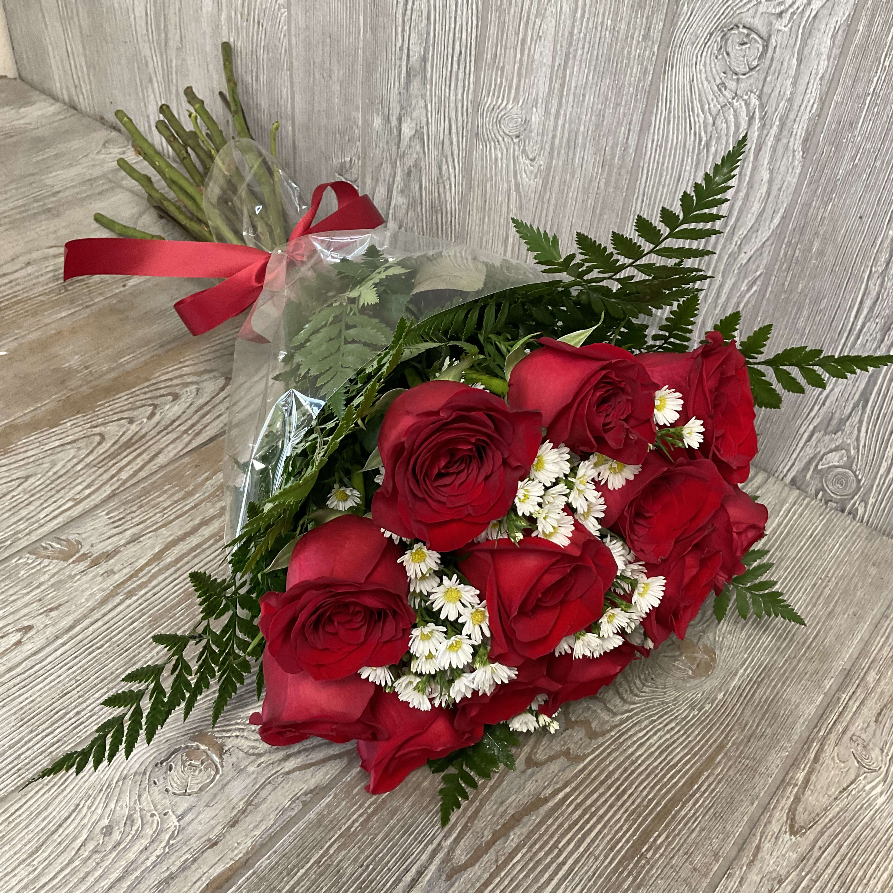Hand-tied bouquet of red roses with small white daisies wrapped in clear cellophane and tied with a red ribbon.
