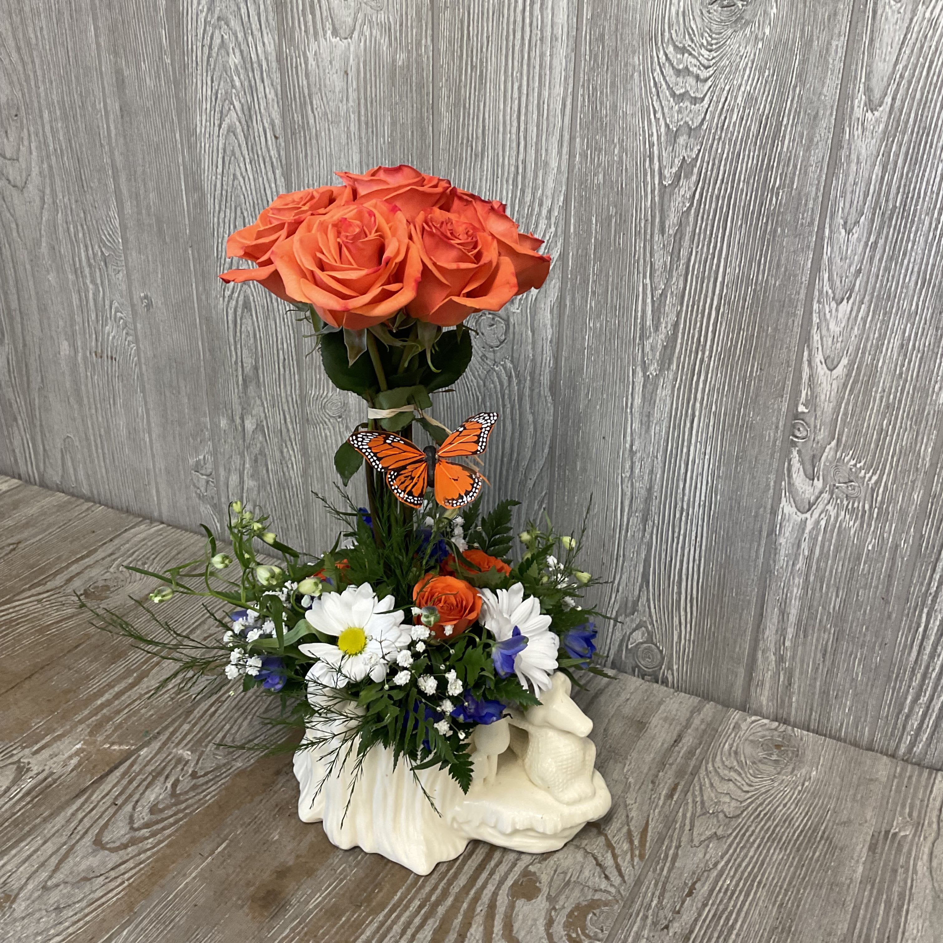 Orange roses in a white ceramic vase with mixed daisies and a butterfly accent
