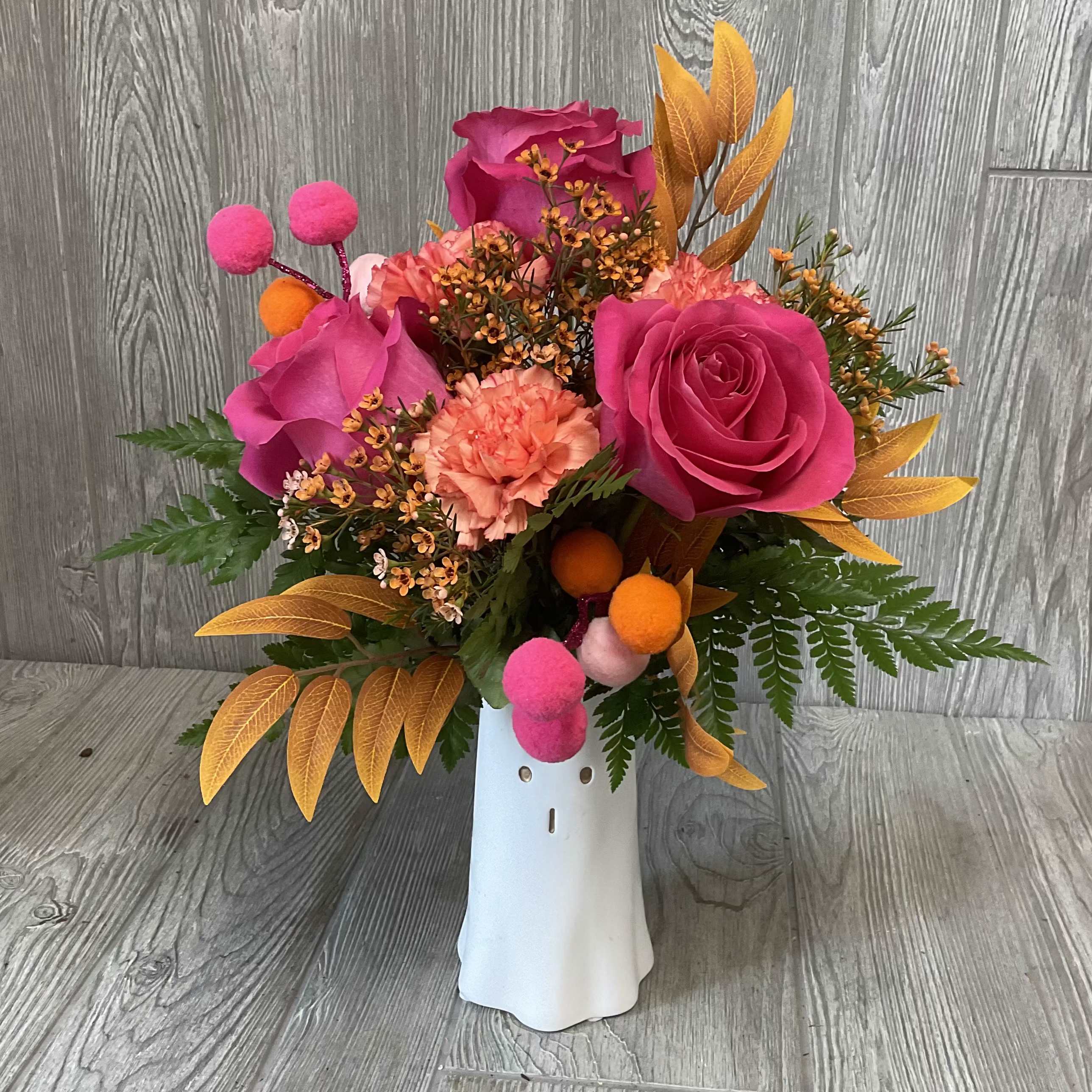 Pink and coral floral arrangement in a white vase with orange accents