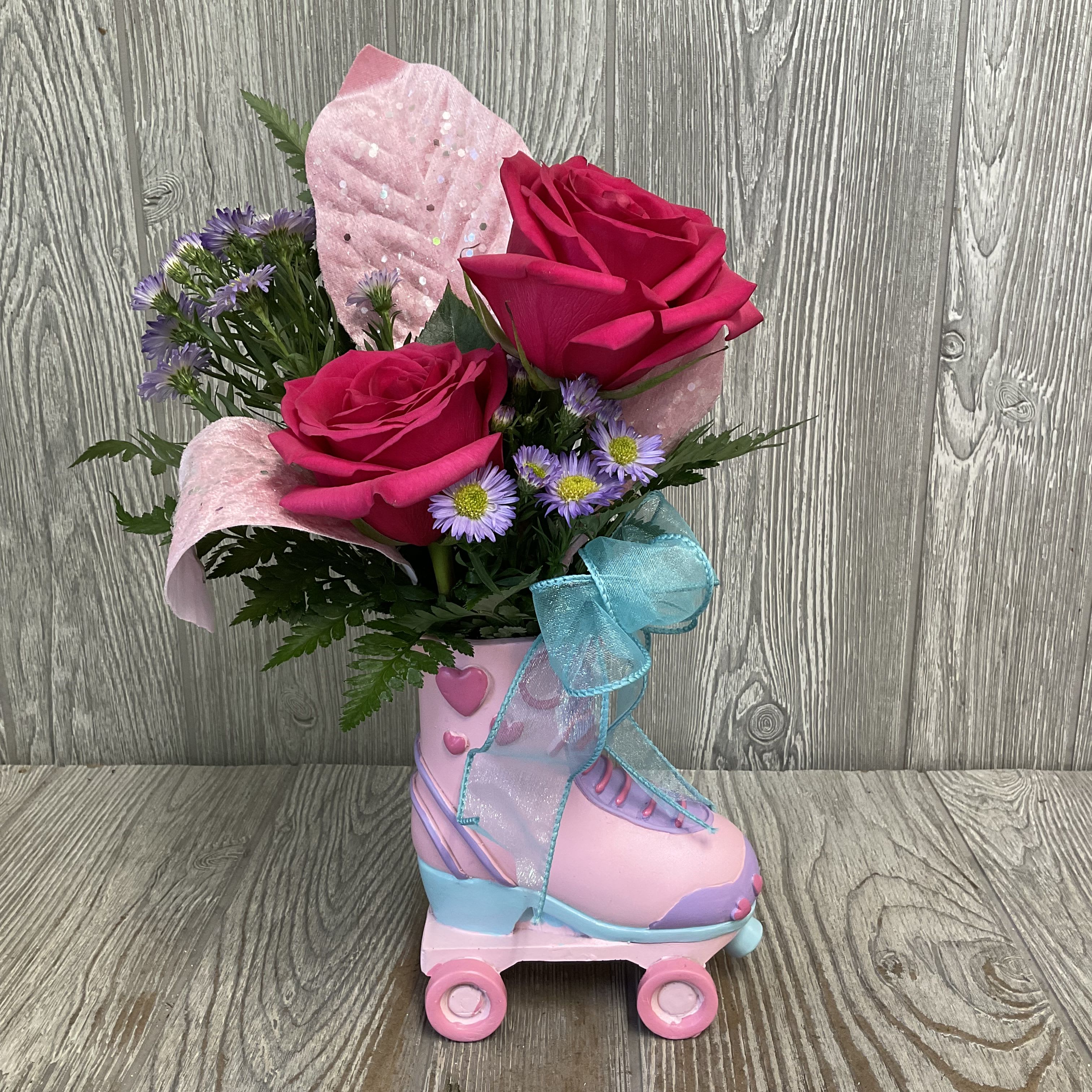Pink roses and purple daisies arranged in a pink roller skate container