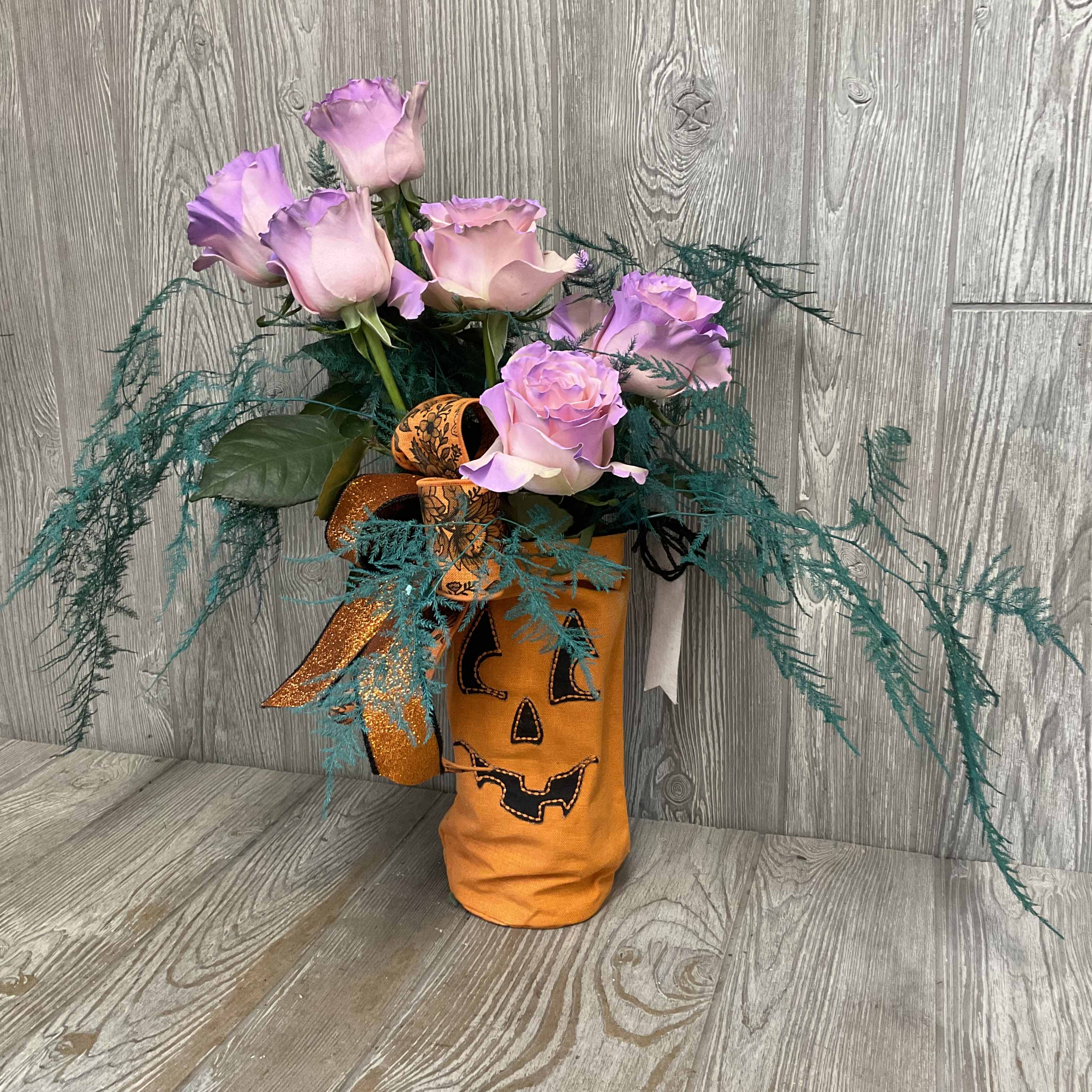 Pink roses in a Halloween pumpkin vase with teal filler and ribbon