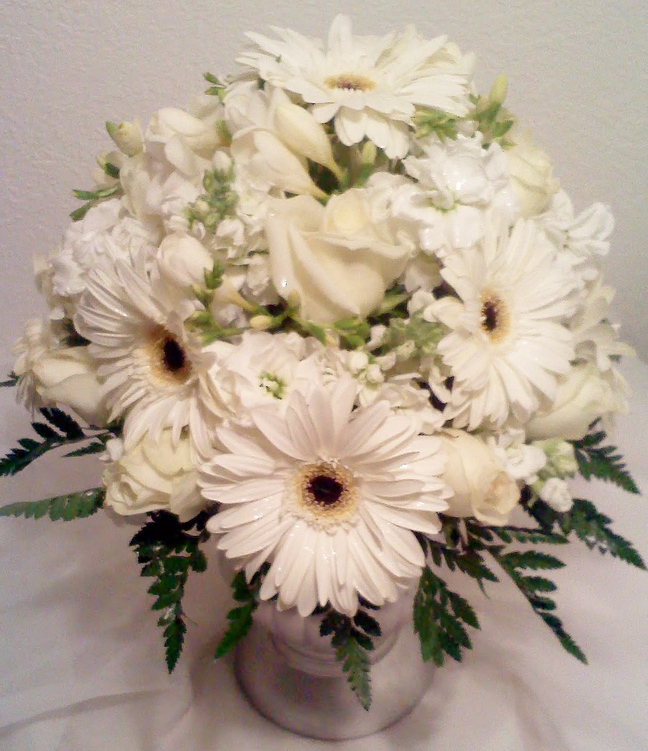 White gerbera daisies and roses arranged in a silver vase