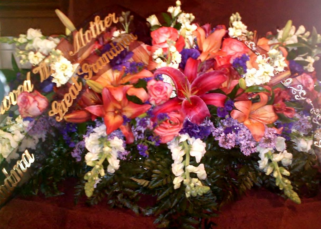 Large funeral spray with lilies, roses, and white flowers with gold script picks