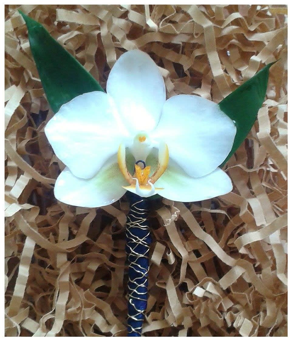White orchid boutonniere with green leaves on a wrapped stem