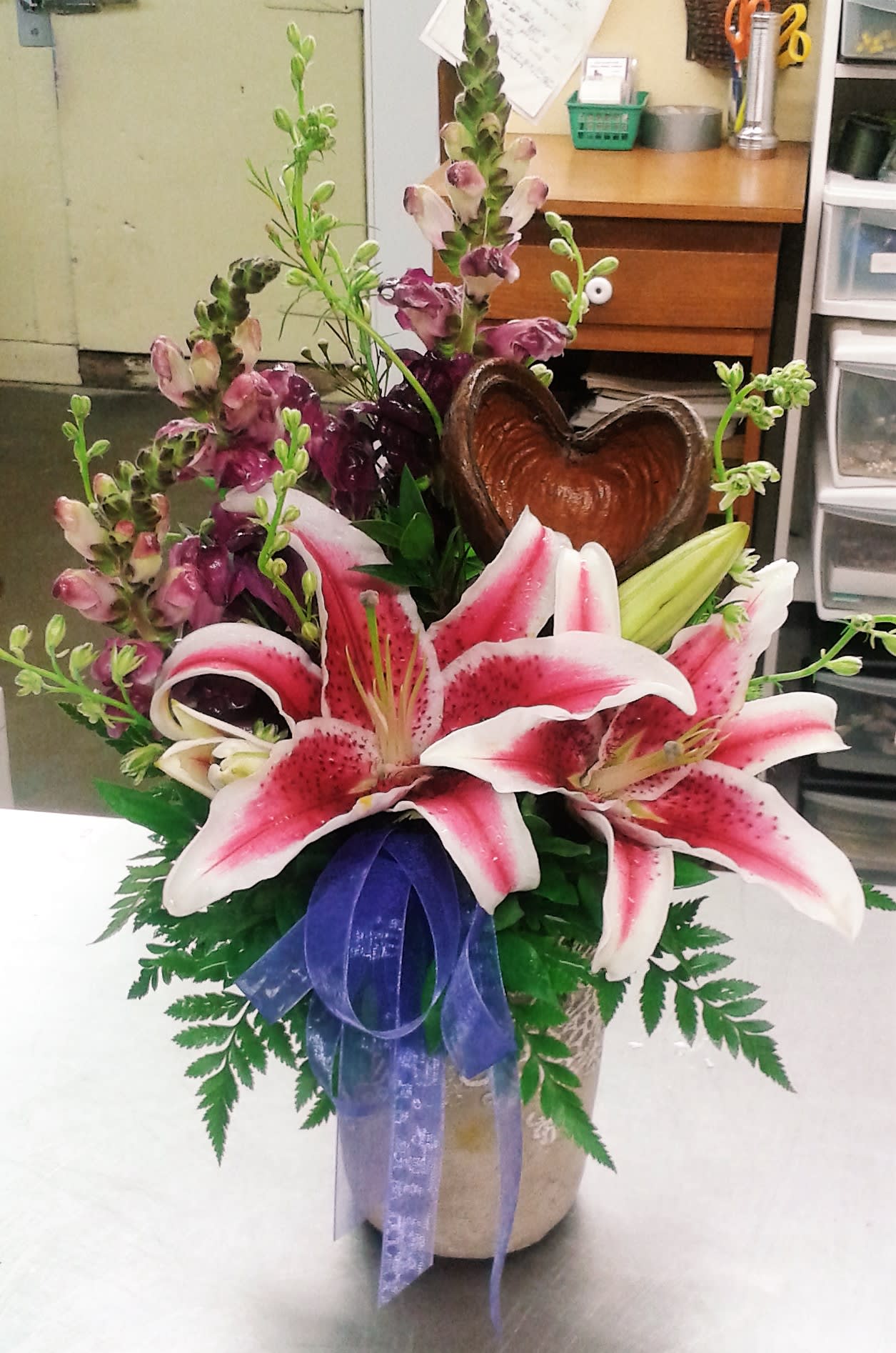 Pink stargazer lilies in a vase with a purple ribbon and heart-shaped accent