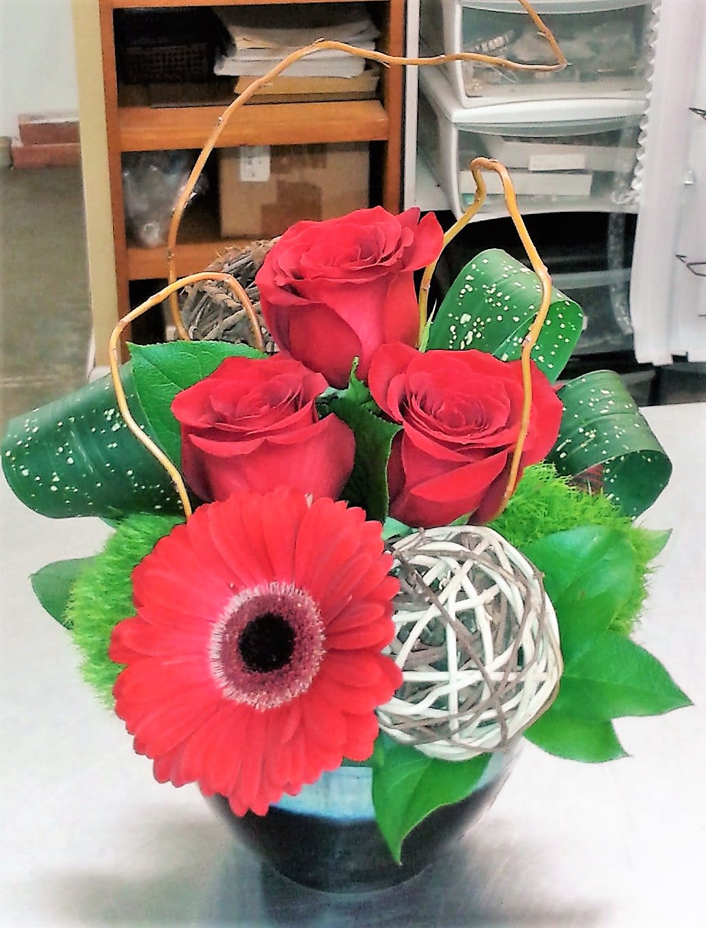 Red roses and a gerbera daisy in a decorative basket arrangement