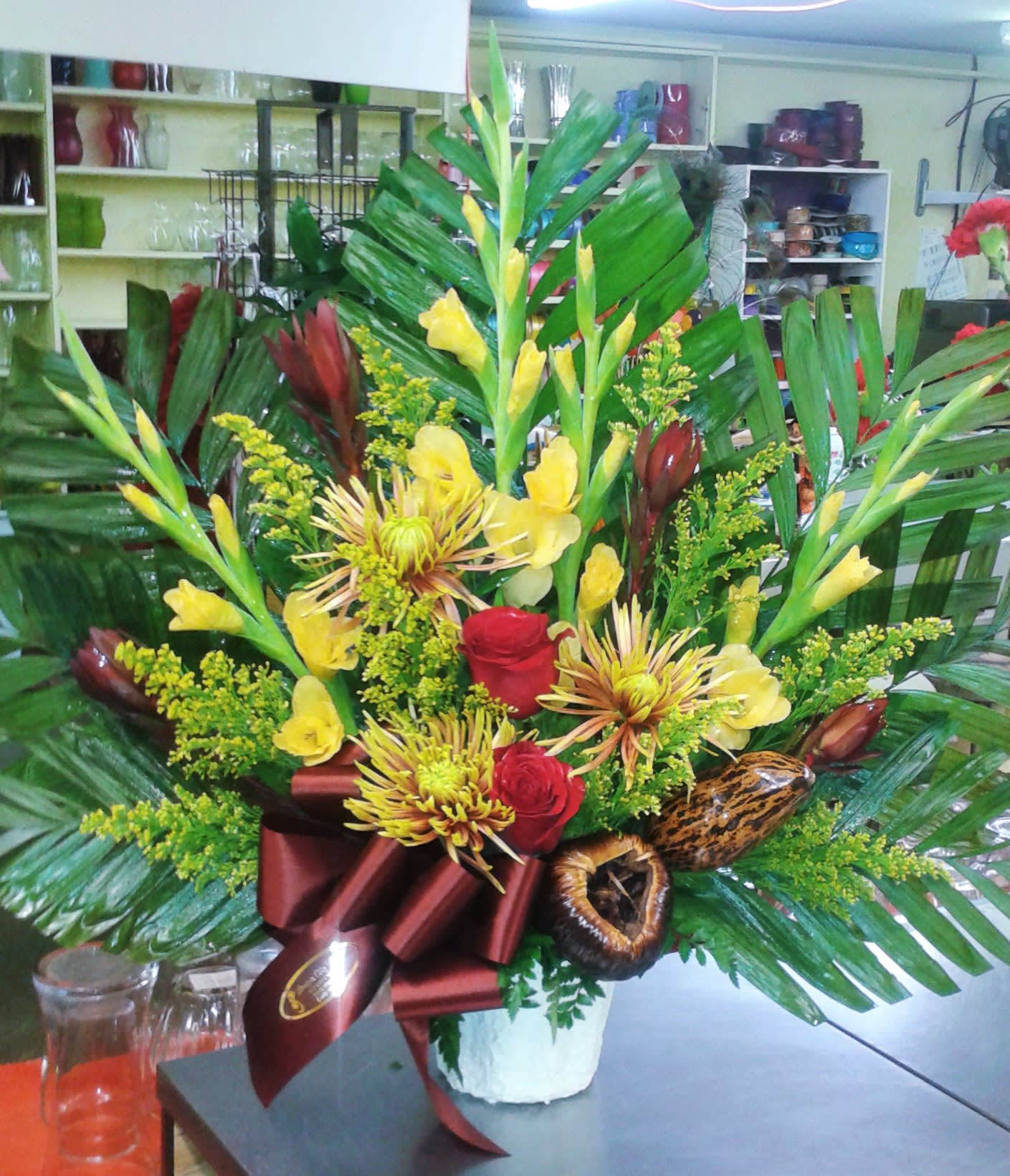 Tropical bouquet with yellow flowers, red roses, and large palm leaves in a white vase