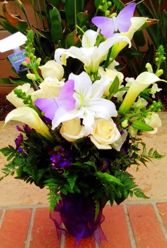 Bouquet of white lilies, cream roses, and purple butterflies in a purple wrap