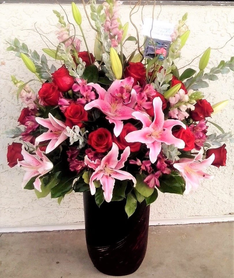 Pink lilies and red roses arranged in a dark vase
