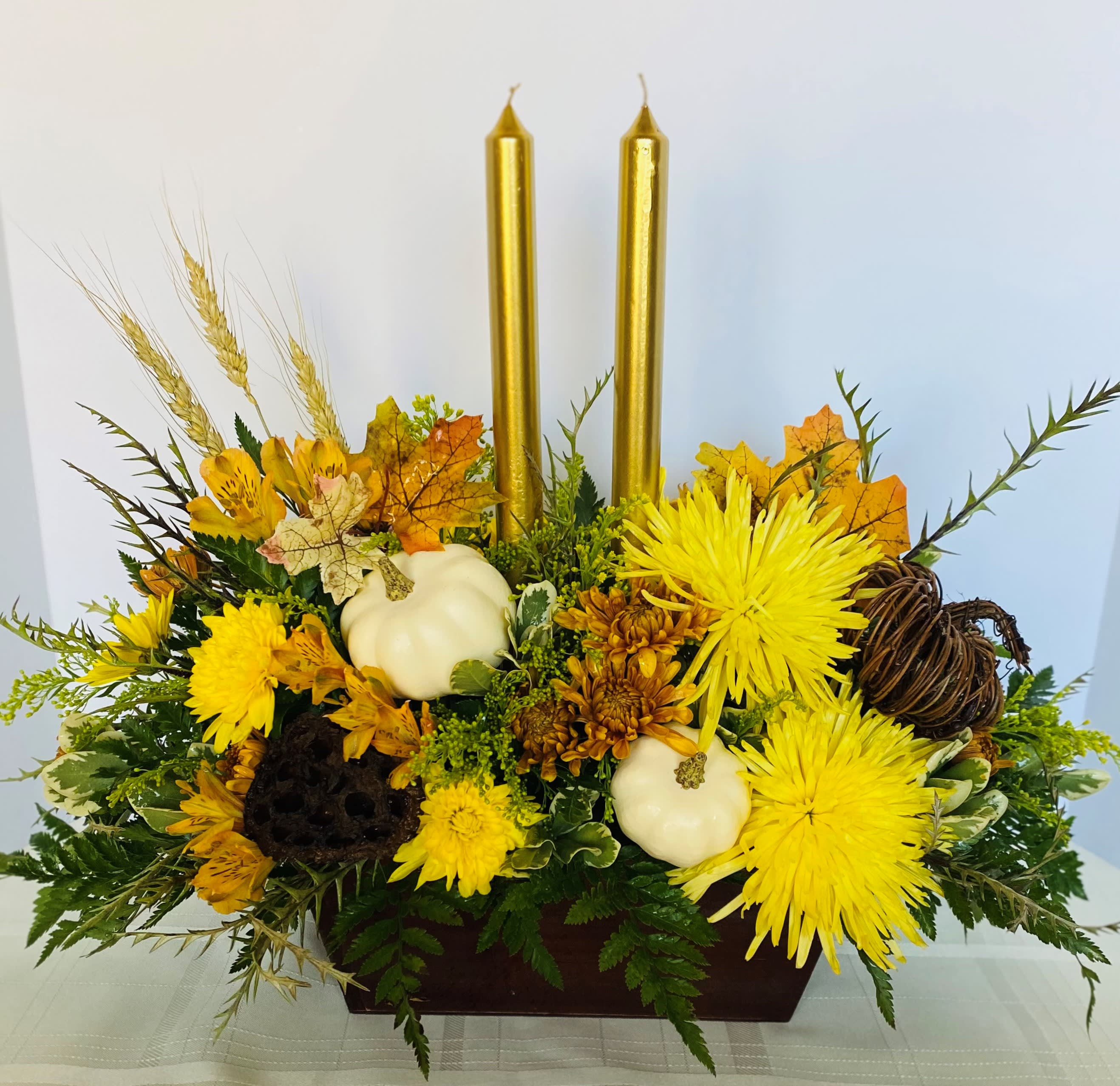 Autumn floral centerpiece with yellow blooms, white pumpkins, and gold candles
