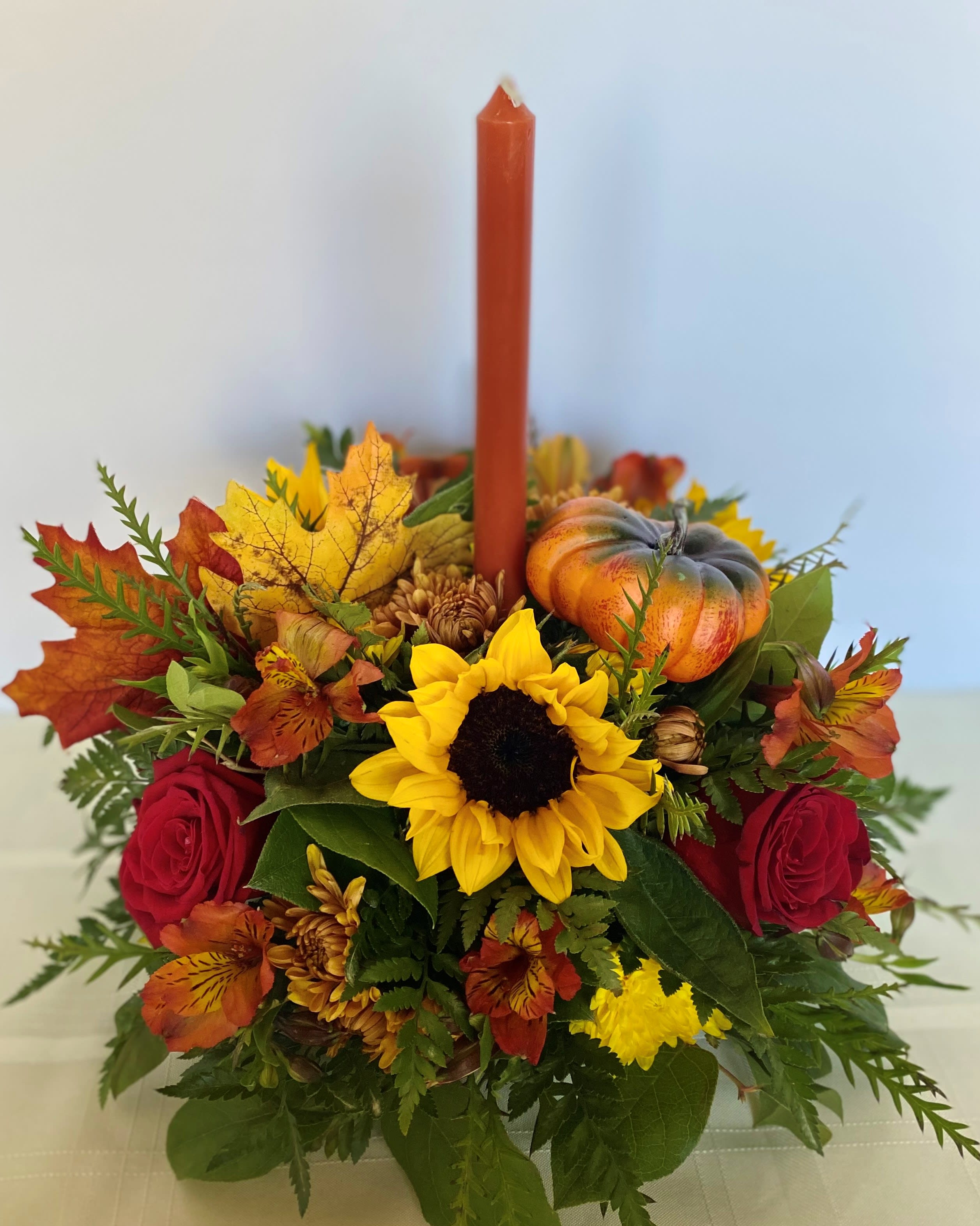 Autumn floral centerpiece with a red candle, sunflower, roses, and a small pumpkin