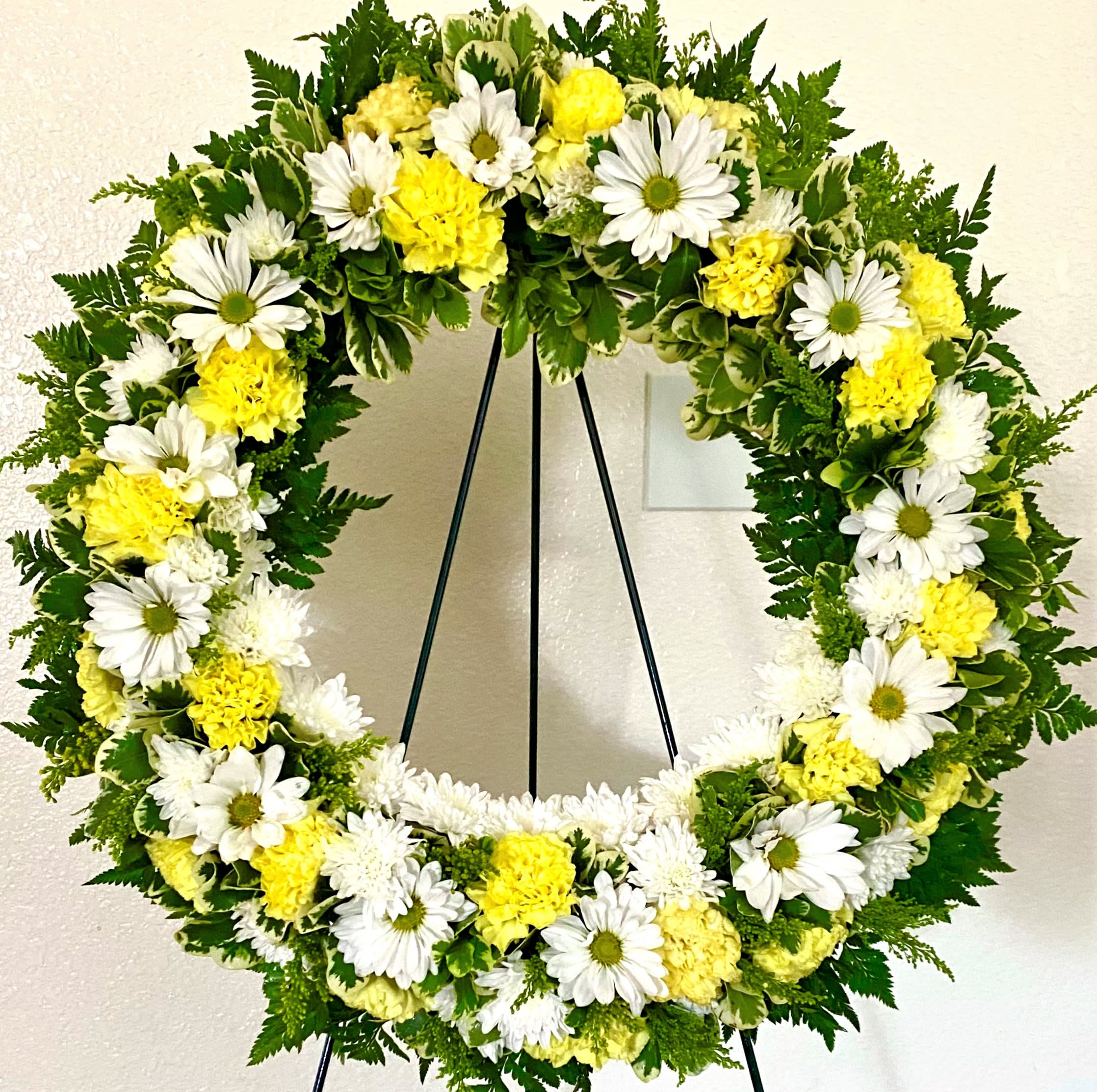 White daisies and yellow carnations arranged in a wreath on a stand