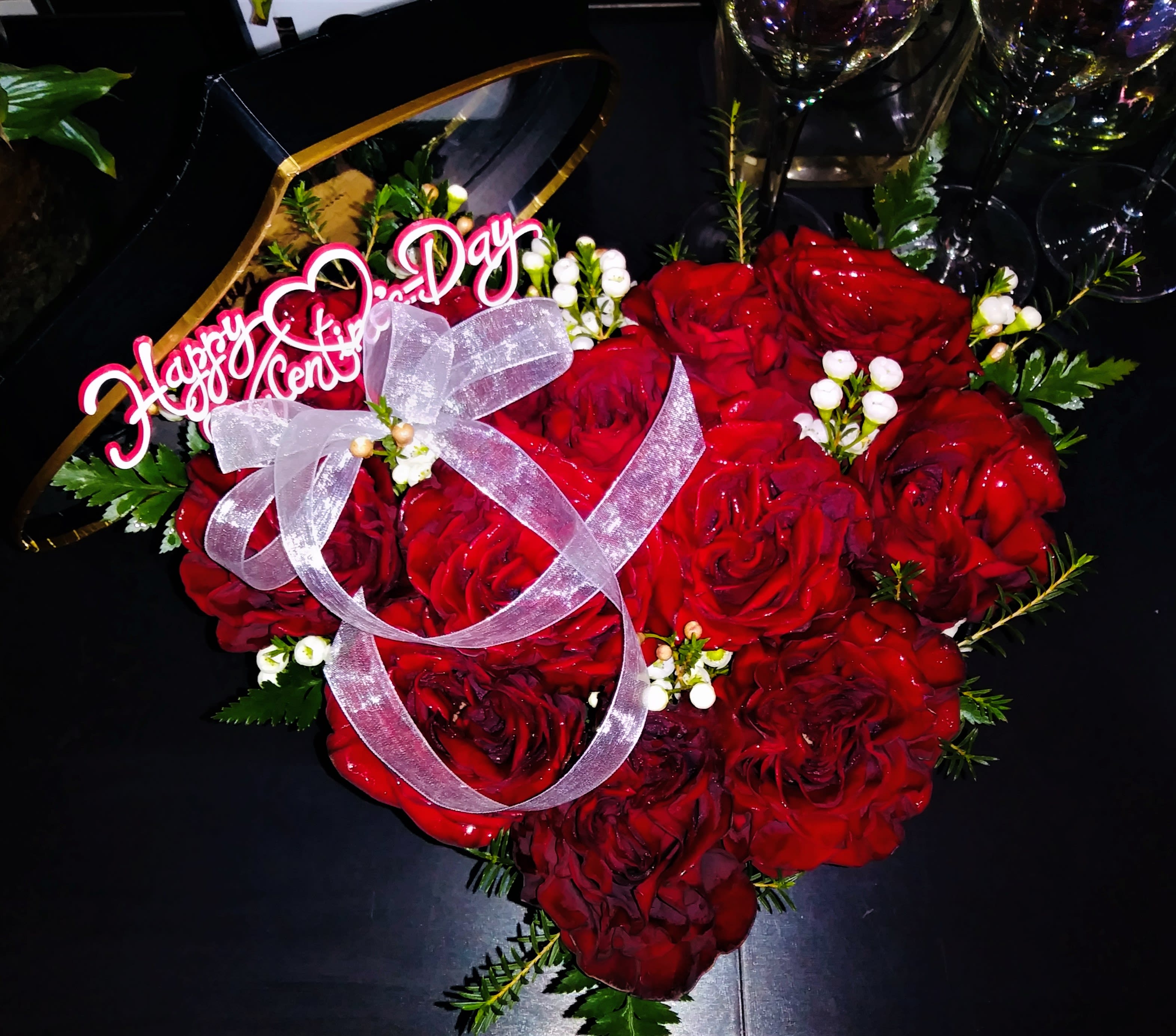 Heart-shaped bouquet of red roses with a pink ribbon and "Happy Anniversary" topper
