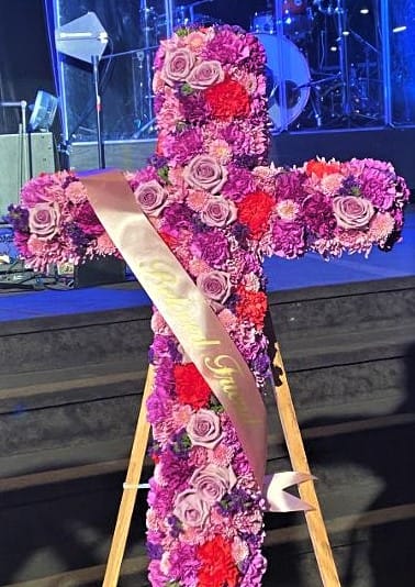 Cross-shaped floral tribute with pink and purple flowers on an easel