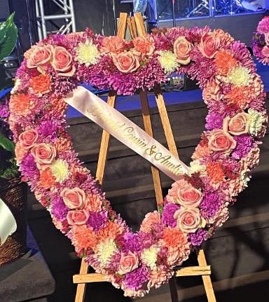Heart-shaped floral wreath with pink roses and purple flowers on an easel