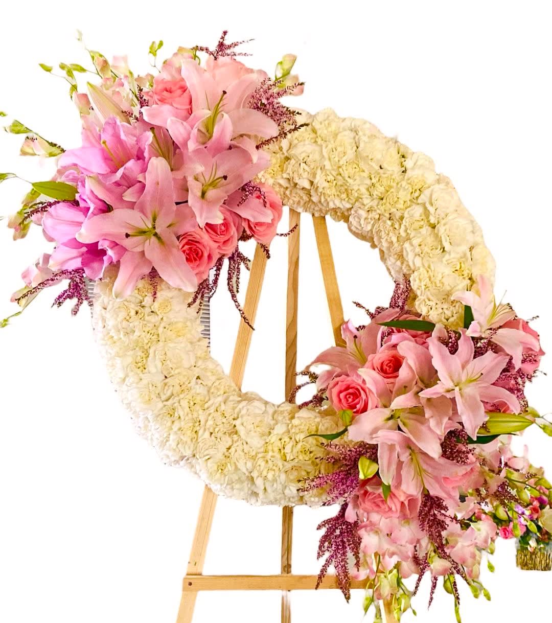 Floral wreath on an easel with pink lilies, roses, and cream flowers