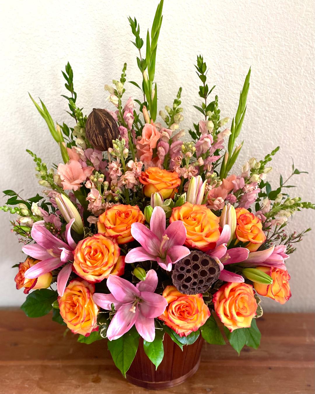 Orange roses and pink lilies in a wooden vase arrangement