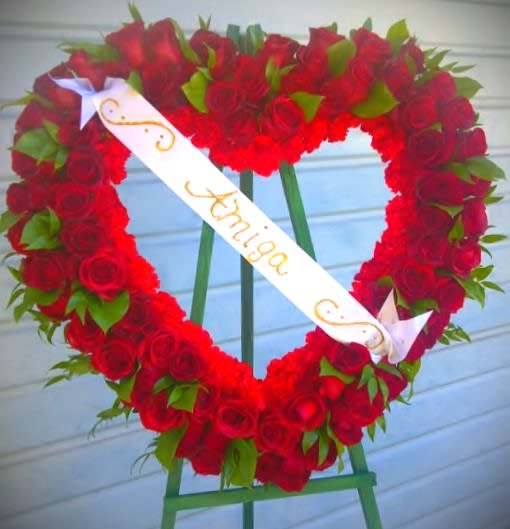 Heart-shaped wreath of red roses with a white ribbon on an easel