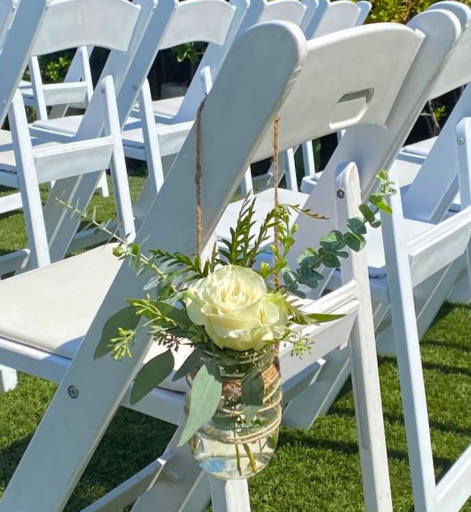 White rose in a small hanging glass vase on a chair