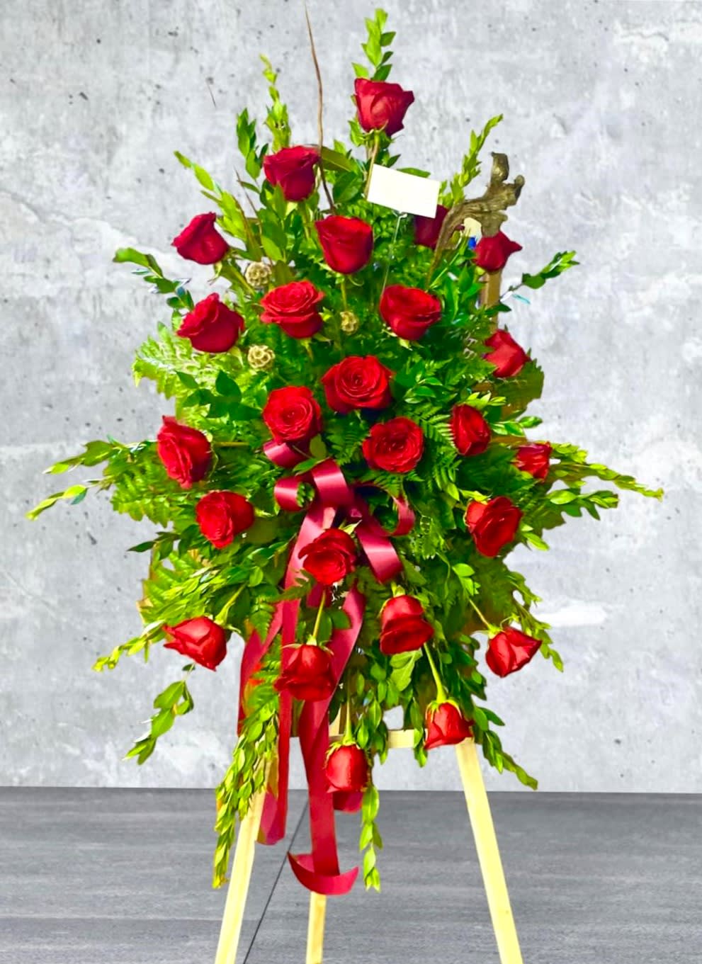 Standing spray of red roses with a pink ribbon on a tripod easel