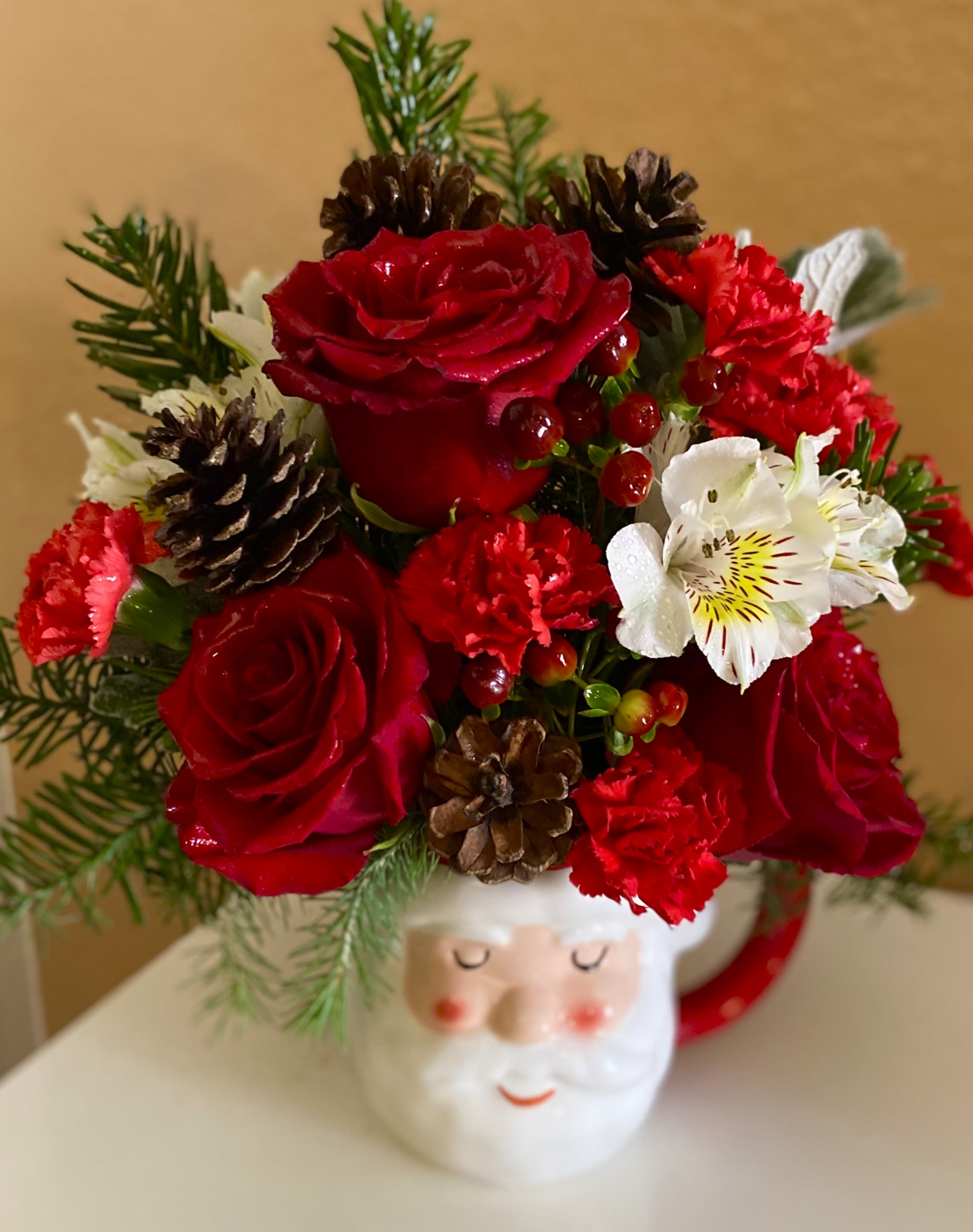 Red roses and carnations arranged in a Santa mug with pinecones.