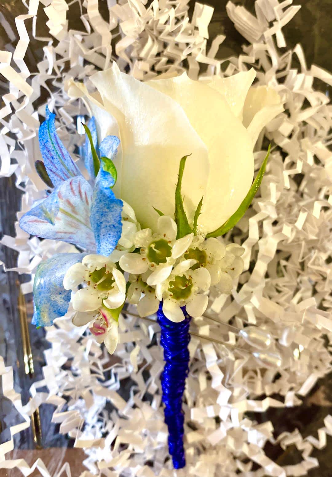White rose boutonniere with blue accent flowers and white filler
