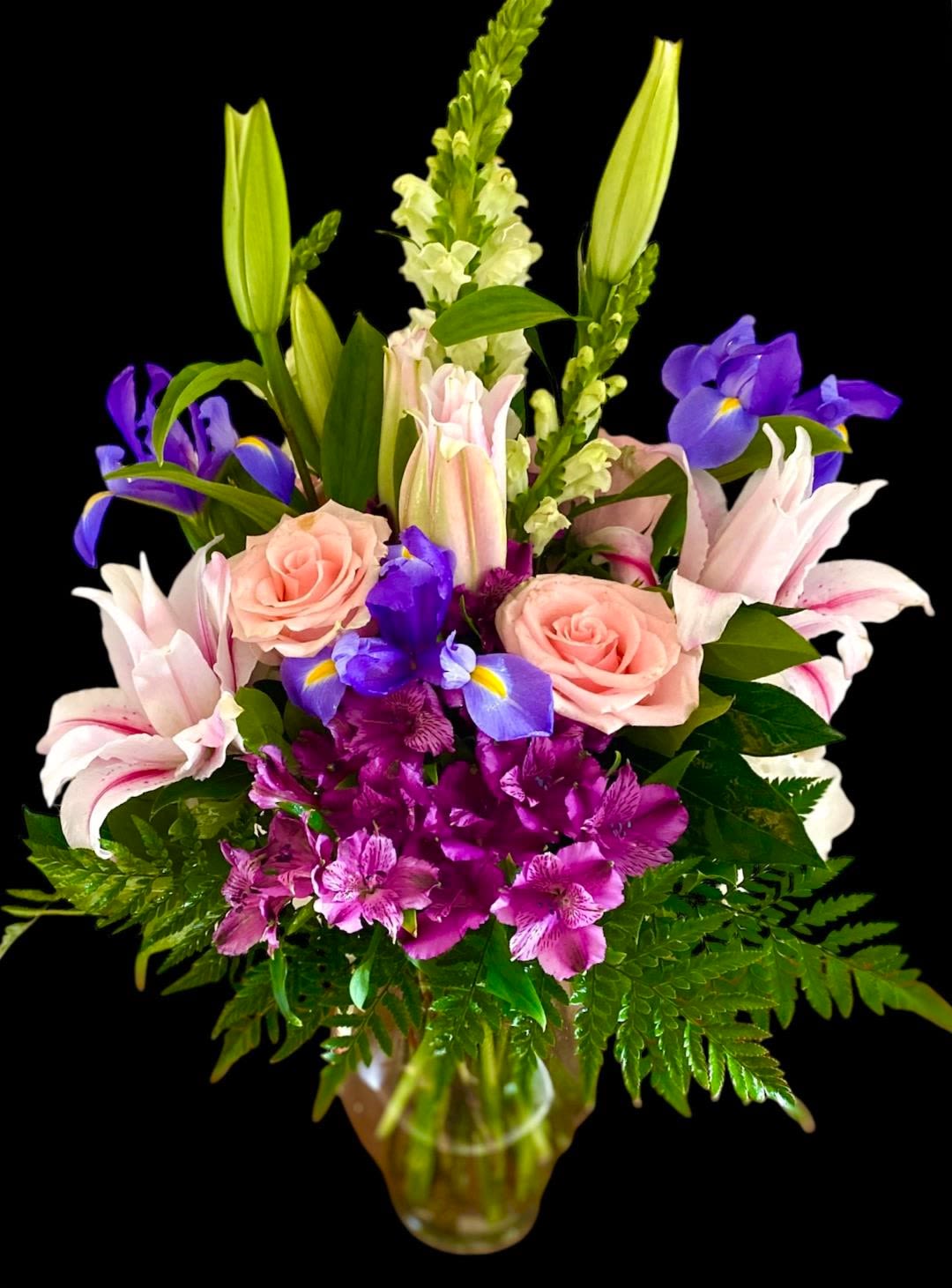 Mixed bouquet with pink roses, lilies, purple irises, and alstroemeria in a glass vase