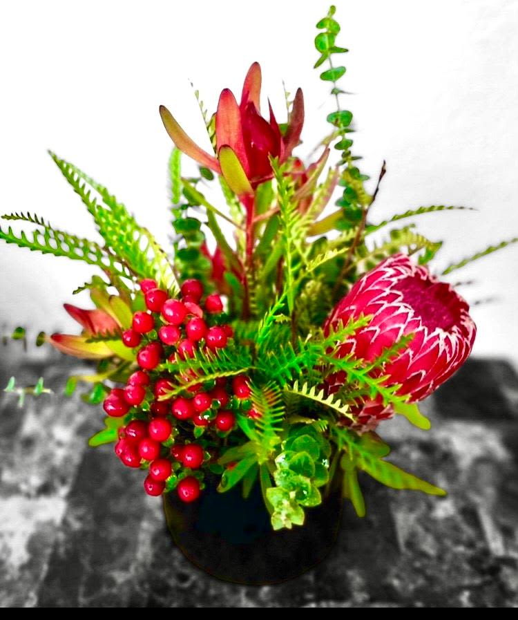 Bright tropical flower arrangement in a black vase with red berries