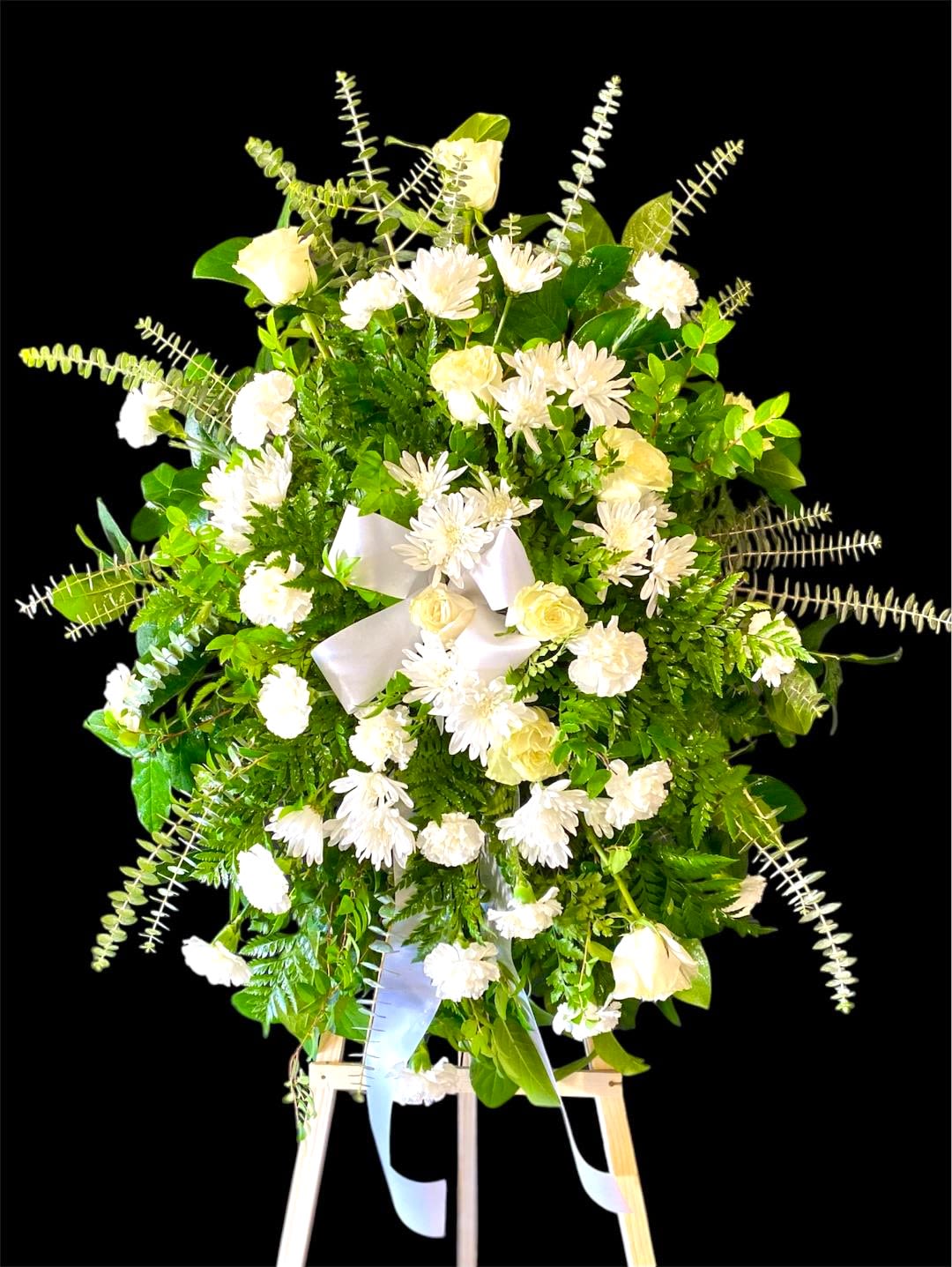 White flowers and greenery arranged on a standing easel with a ribbon