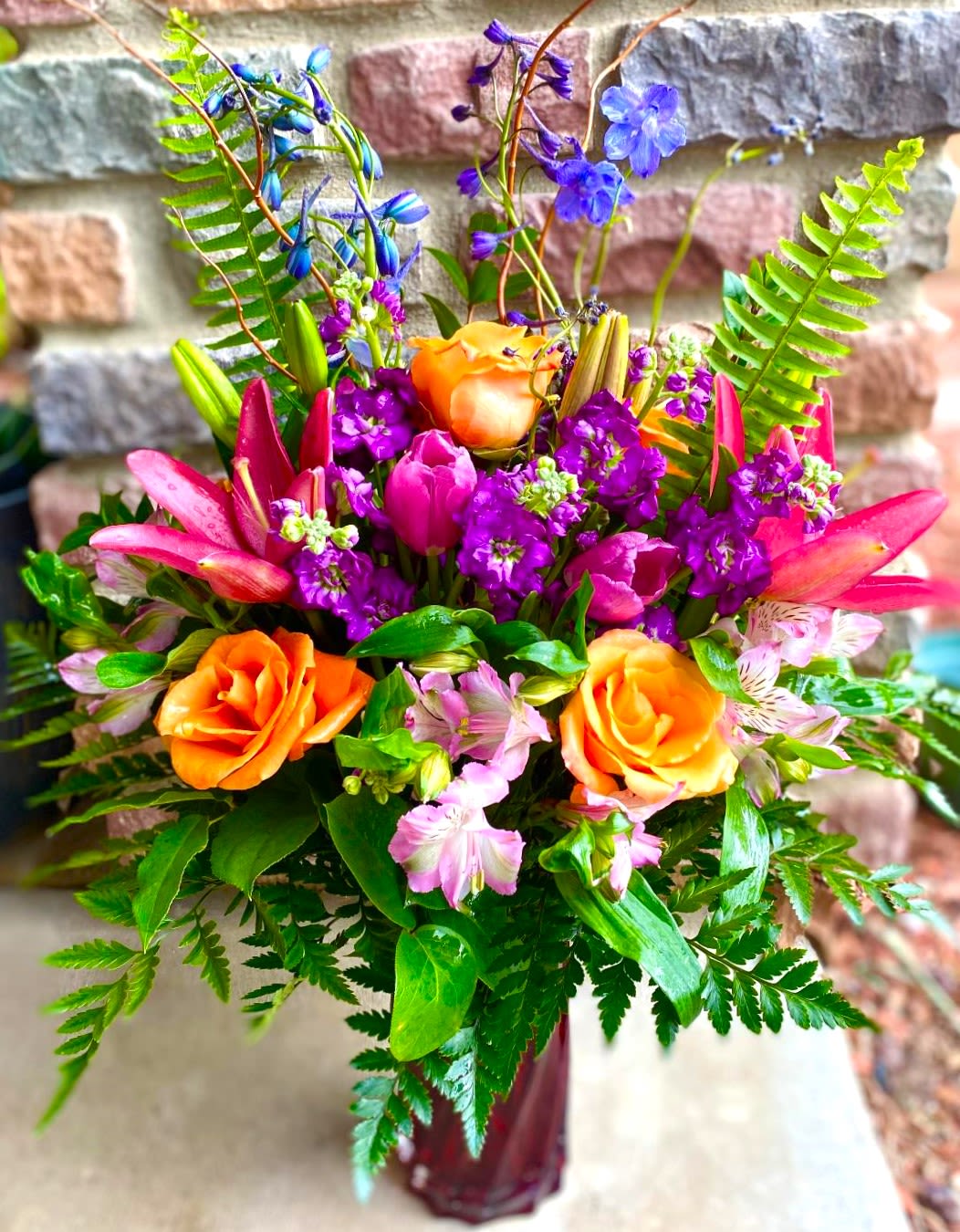 Colorful bouquet of orange roses, pink lilies, and purple flowers in a vase