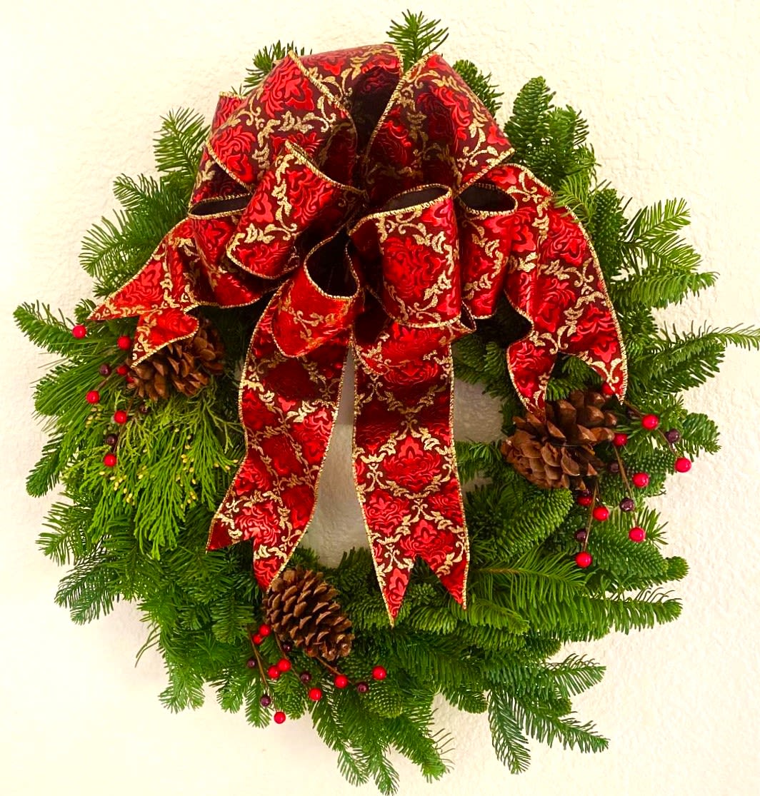 Christmas wreath with a red patterned bow, pinecones, and evergreen branches