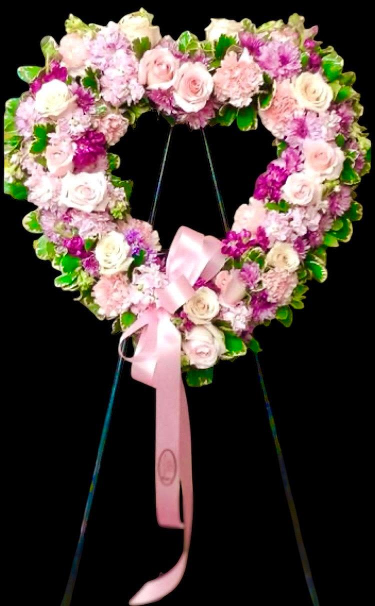 Heart-shaped floral wreath with pink roses and a pink ribbon on a stand